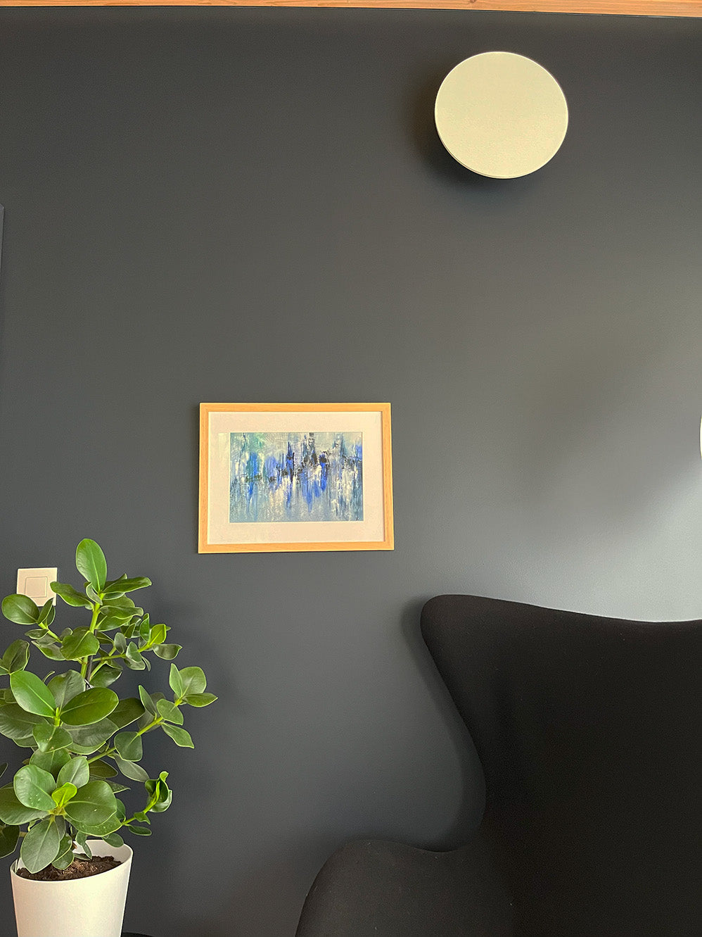 Watercolour Abstract called Drift hanged on a dark blue wall with plant and light