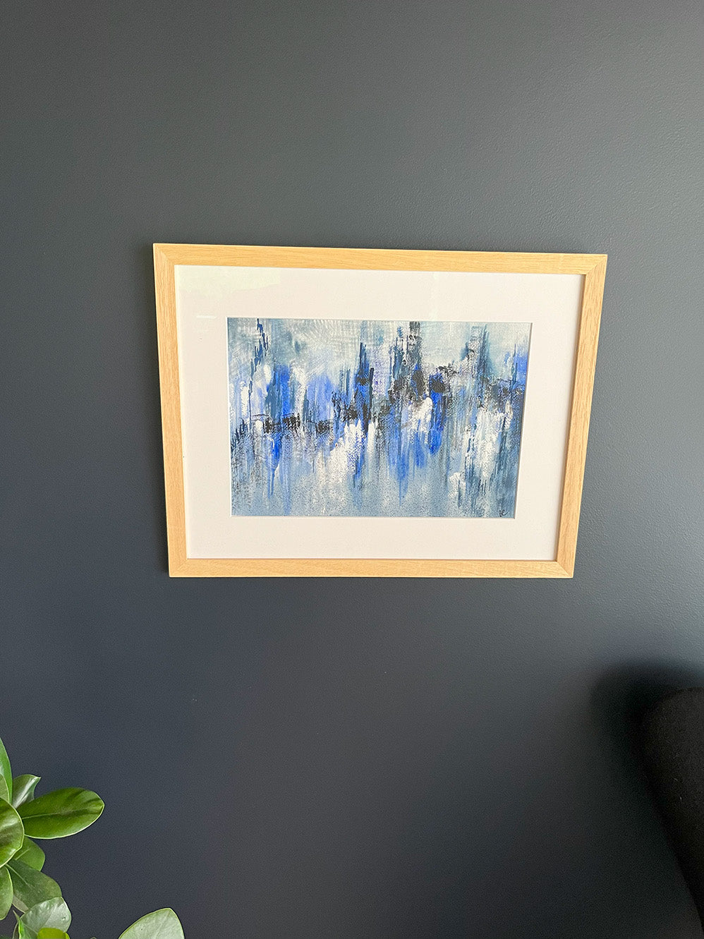 Watercolour Abstract called Drift hanged on a dark blue wall with plant