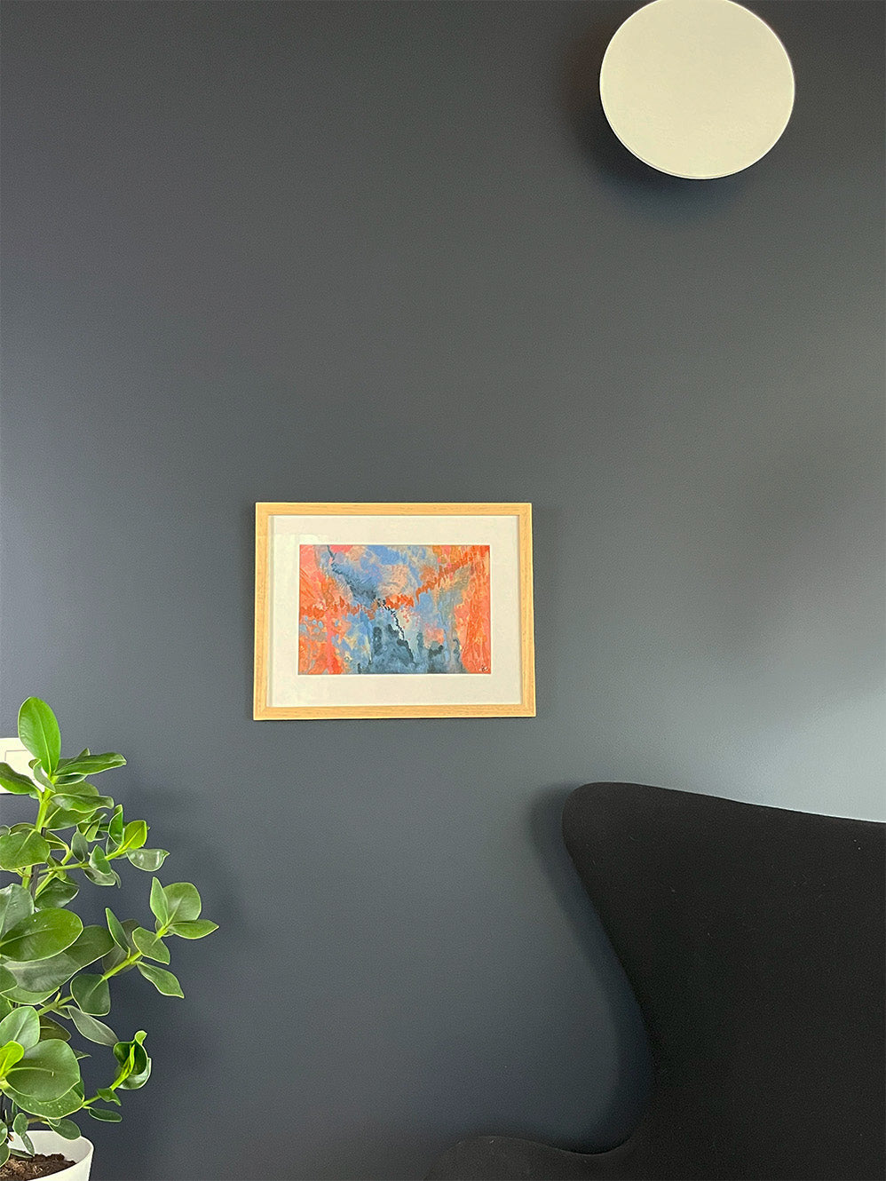 Framed Watercolour Abstract called Conundrum hanged on a dark blue wall with light and plant