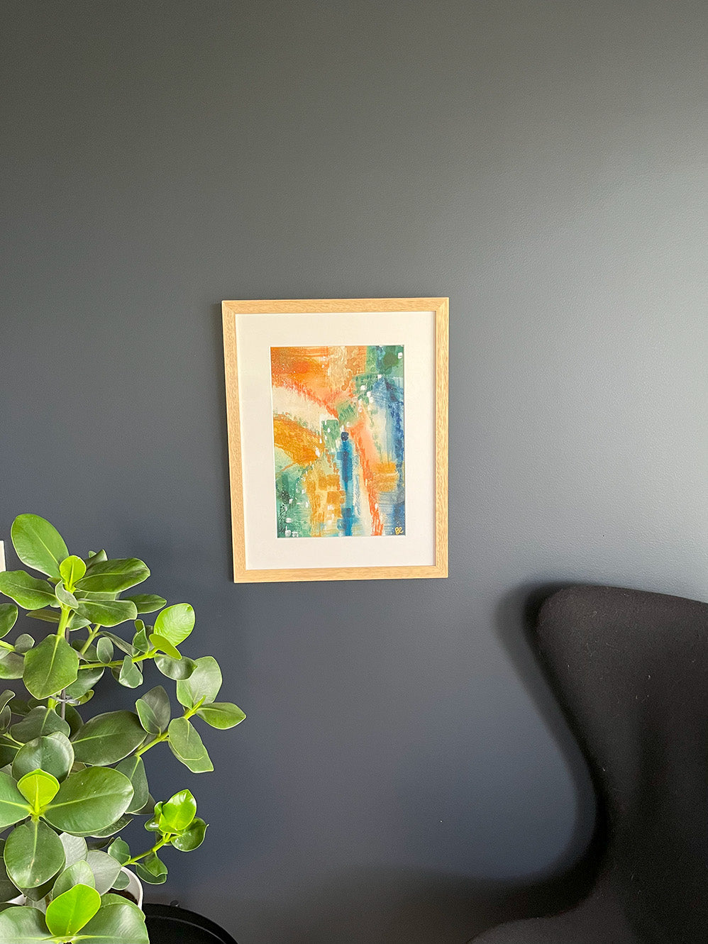 Framed Watercolour Abstract called Yearning hanged on a dark blue wall with plant