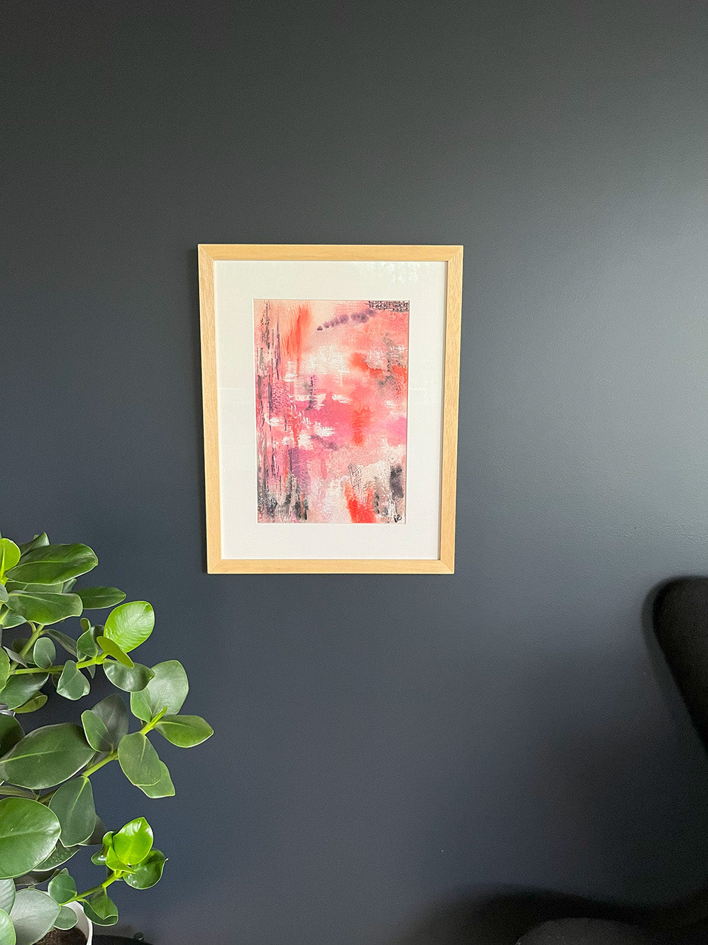 Framed Watercolour Abstract called Uplift hanged on a dark blue wall with plant