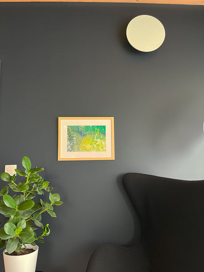 Framed Watercolour Abstract called Tenacity hanged on a dark blue wall with plant and light